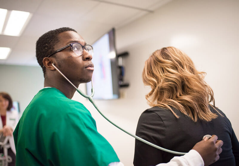 A student uses a stethoscope to listen to a woman's back
