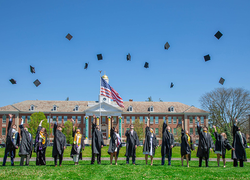 Students in graduation gowns throw their caps in the air on the Siena campus.