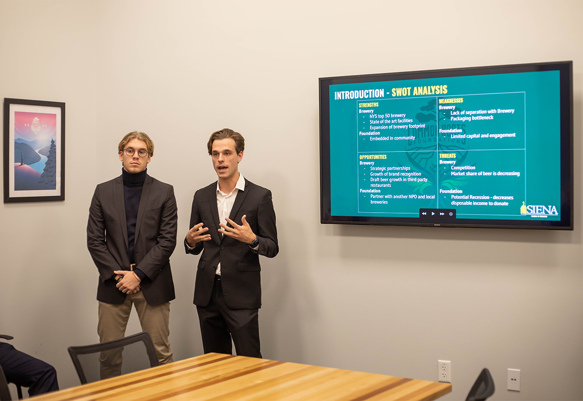 Two male students in suits present a SWOT analysis to a class in a conference room.