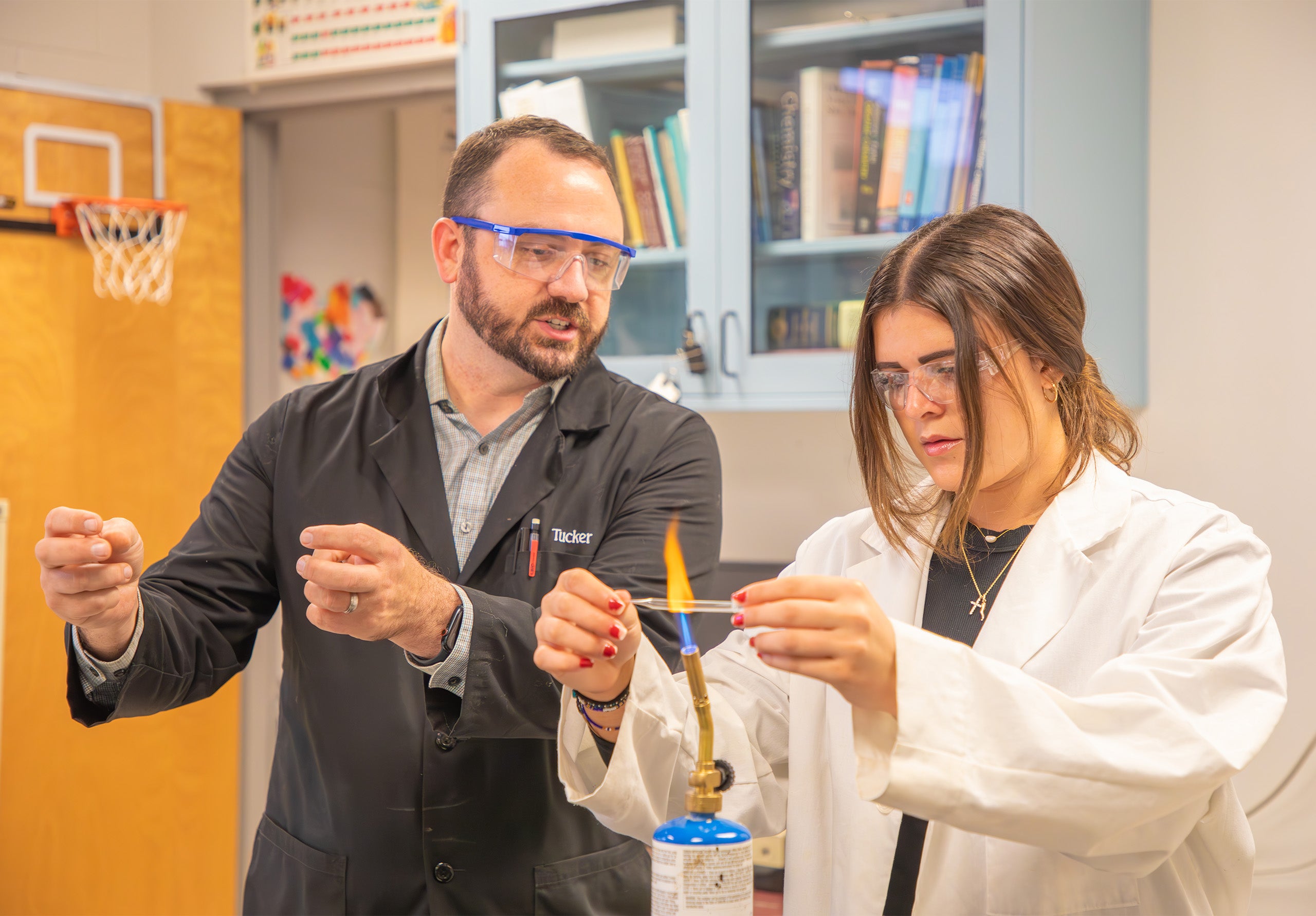 A Professor talks to a student in a chemistry lab while holding beakers